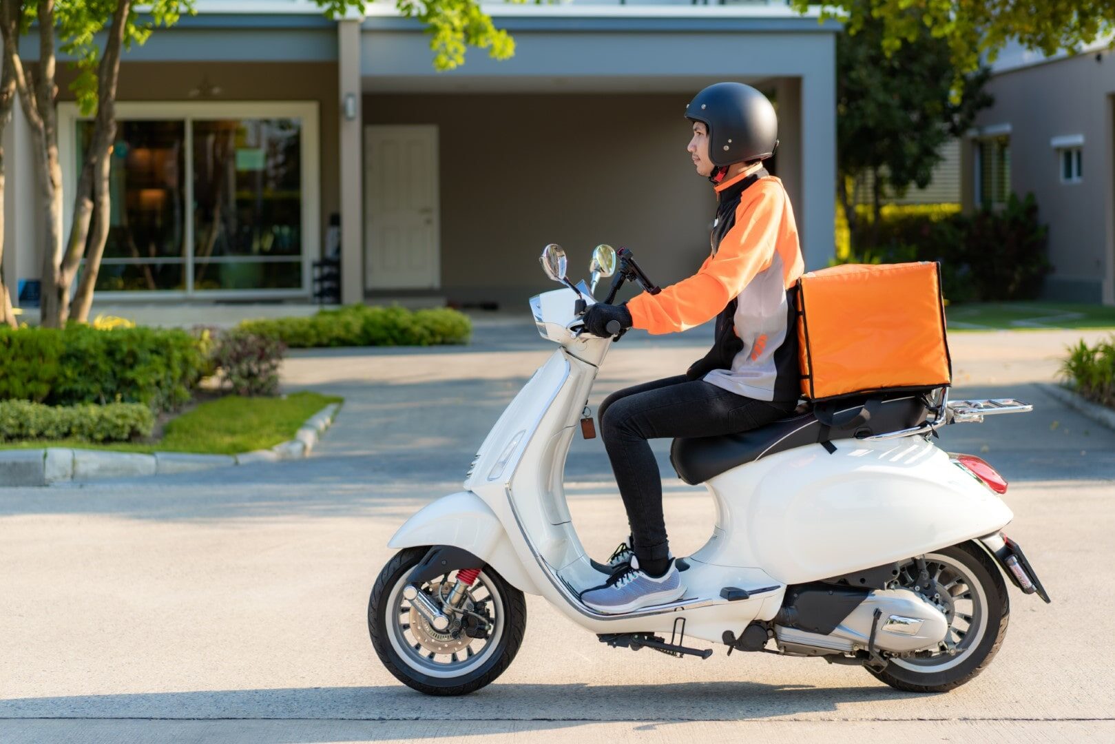 Asian man courier on scooter delivering food in town streets wit