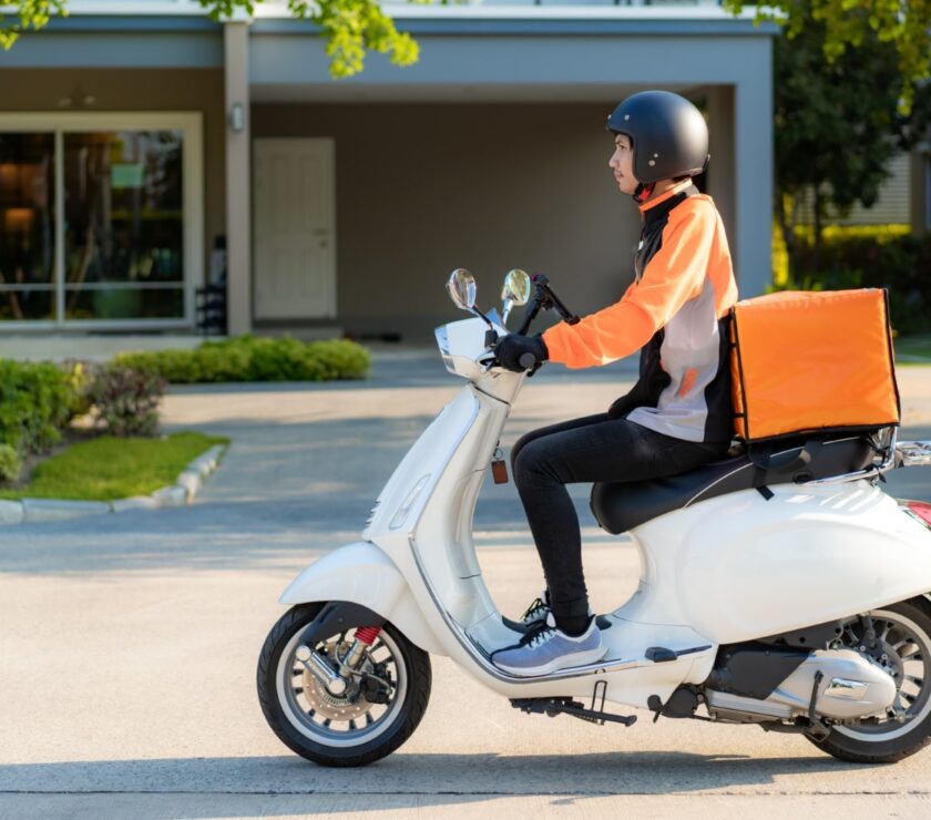 Asian man courier on scooter delivering food in town streets wit